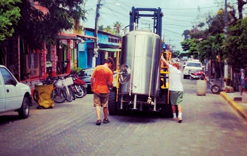 Photo of Greenberg and an associate walking with a forklift that's carrying brewing equipment through San Juan del Sur, Nicaragua.