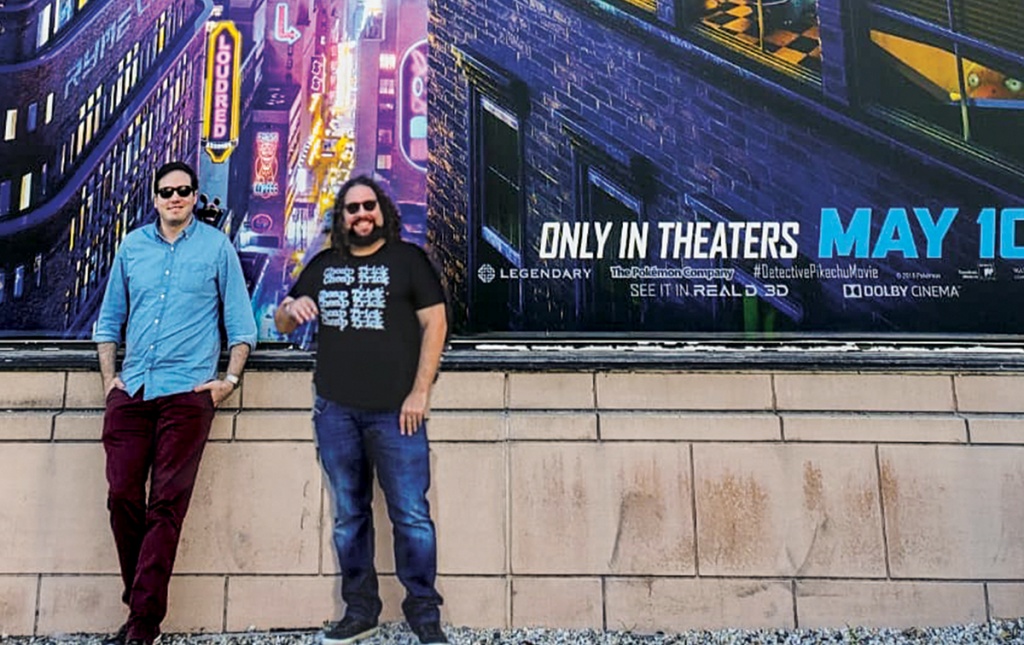 Dan Hernandez ’06 and Benji Samit ’06 standing in front of a Pokémon: Detective Pikachu poster