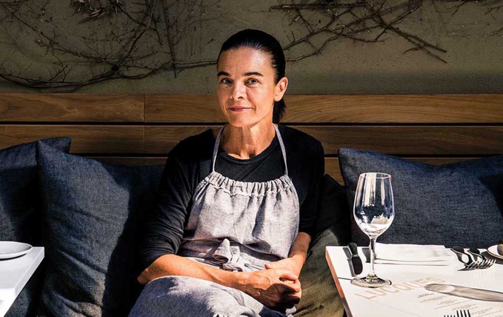 Photo of Suzanne Goin by Julia Stotz sitting on a bench behind a table at her restaurant.