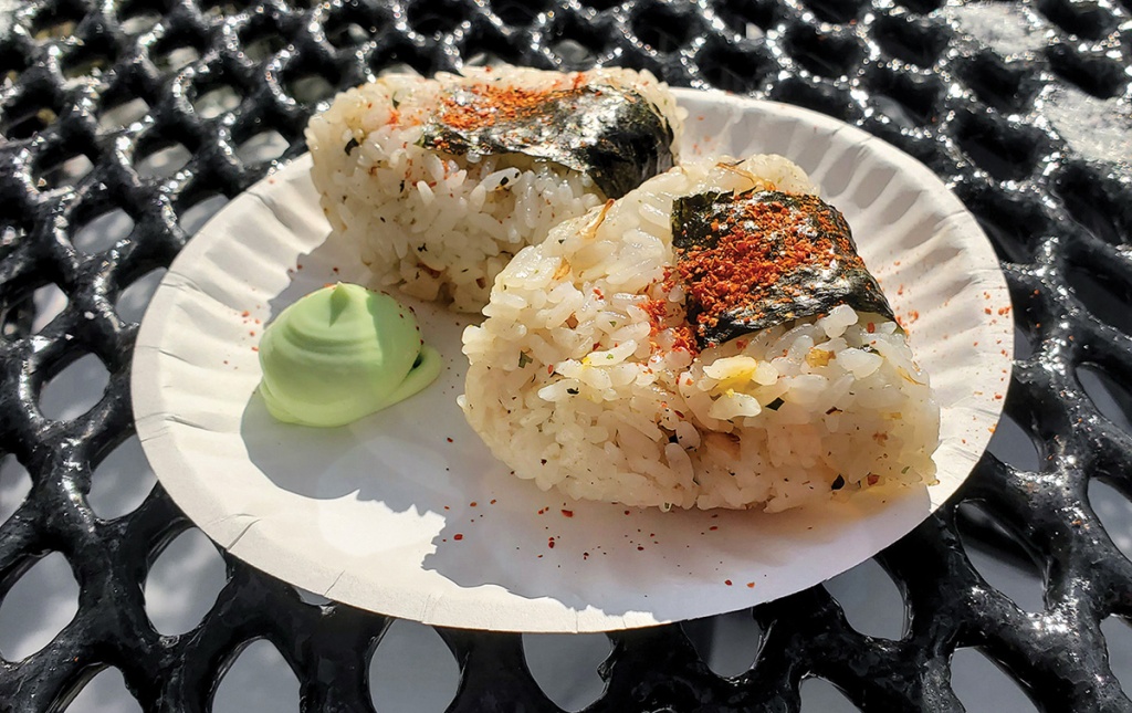 Image of onigiri on a paper plate with wasabi on an outside table