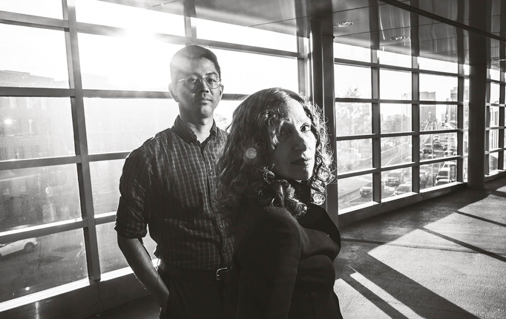 Image of Tony Thaweethai and Andrea Goldin Foulkes standing in front of a wall of windows looking at the camera.