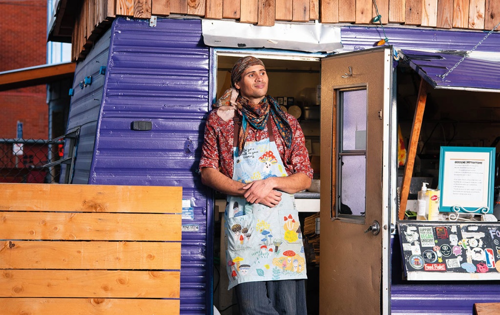Image of Alkebulan Moroski standing in the door of a food trailer wearing an apron.