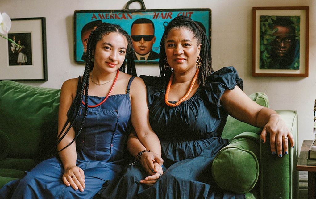 Image of Ruby Aiyo Gerber and her mother Lynn Nottage on a couch holding hands with paintings in the background.