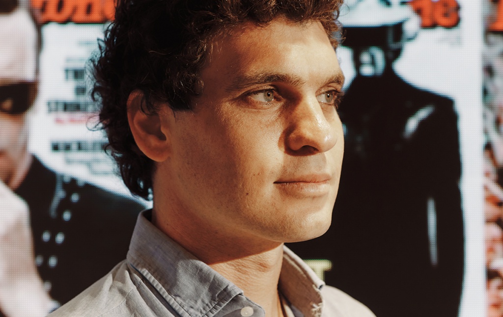 portrait of Gus Wenner in front of a wall of Rolling Stone covers