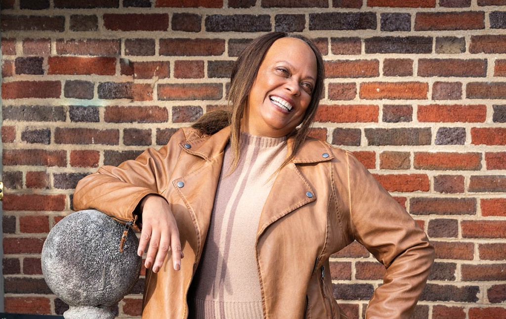 Image of Brenda Barbour smiling with her hand on her hip and a brick wall. 