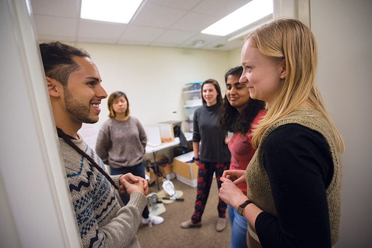 A photograph of a group of people chatting in a classroom.