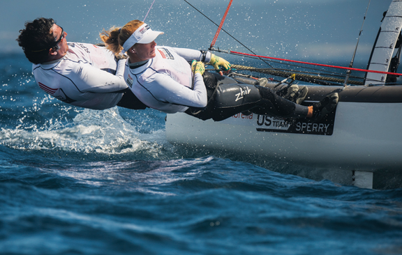 Photograph of two sailors leaning out of a boat on the ocean.