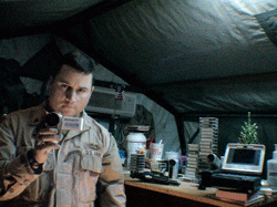 Photo of a man in partial military uniform pointing his video camera in a mirror.