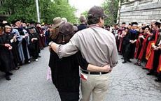 Photo of two people walking at commencement with their arms around each other.