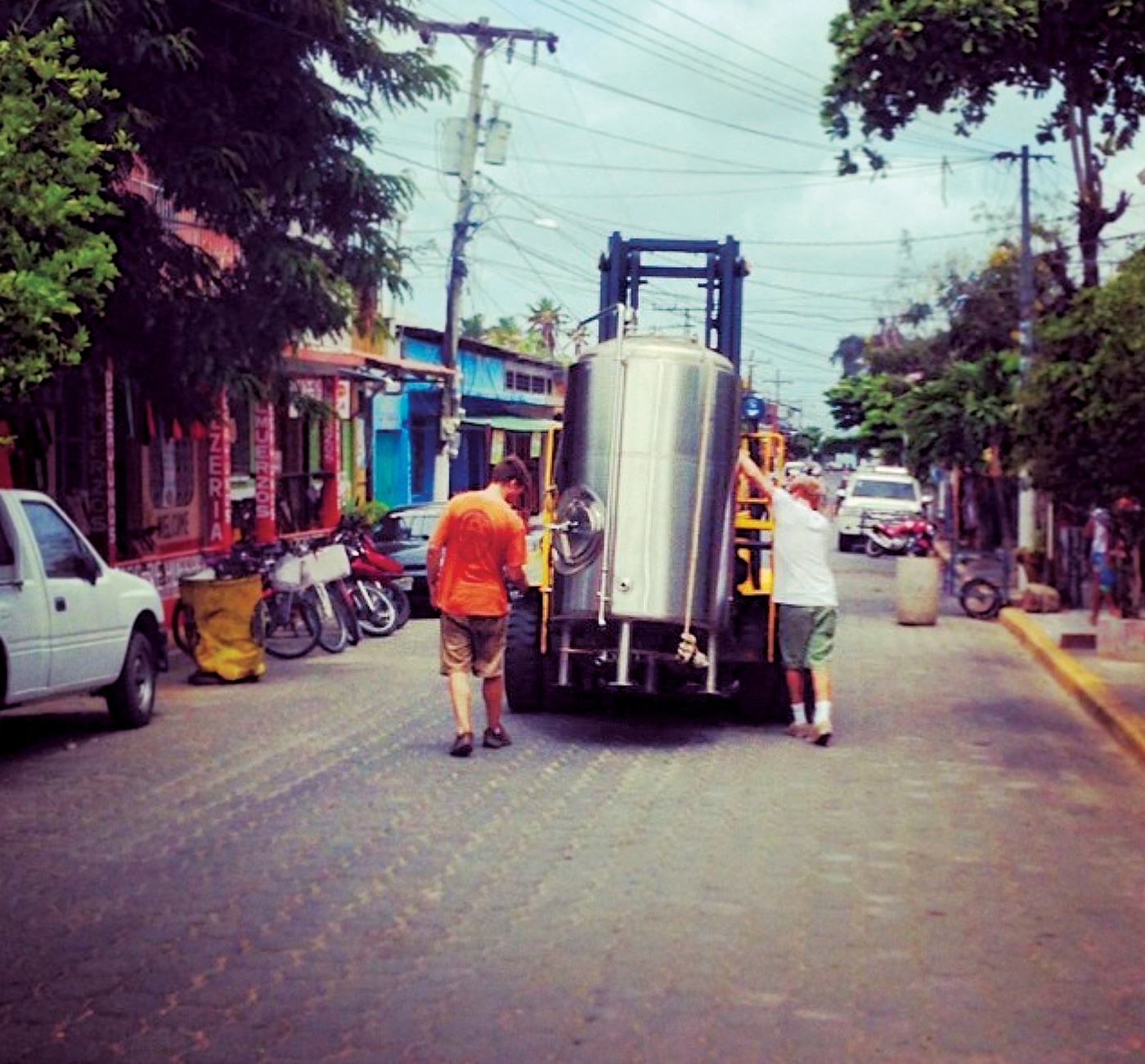 Photo of Greenberg and an associate walking with a forklift that's carrying brewing equipment through San Juan del Sur, Nicaragua.