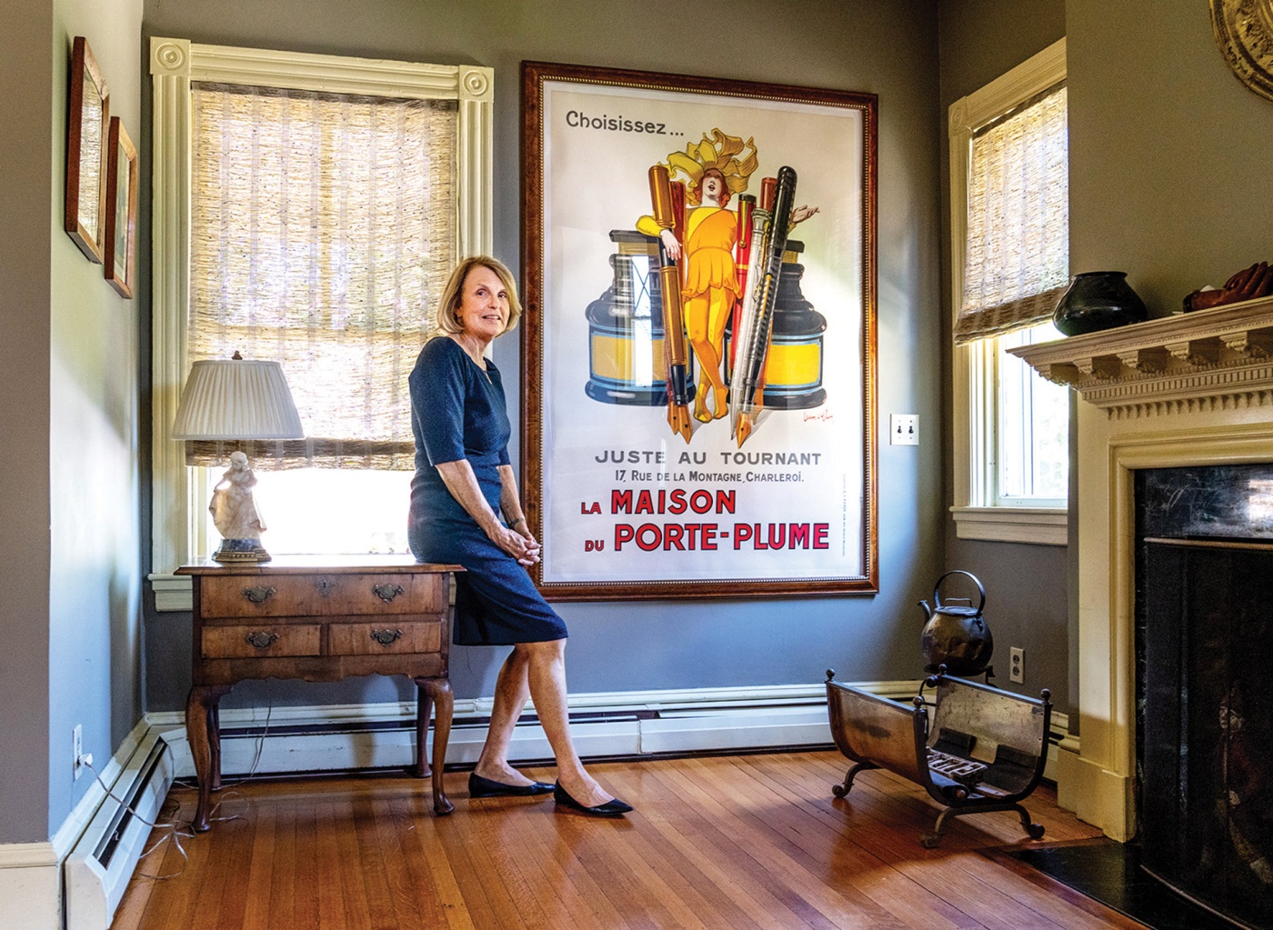 Image of Tracy Breton in her home leaning on a table with a fireplace in the foreground.