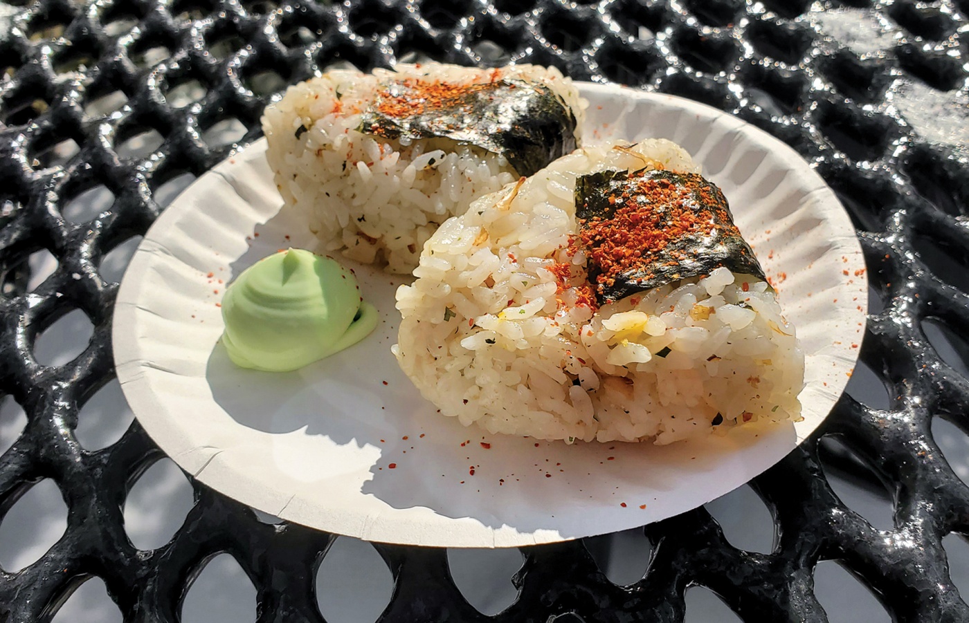 Image of onigiri on a paper plate with wasabi on an outside table