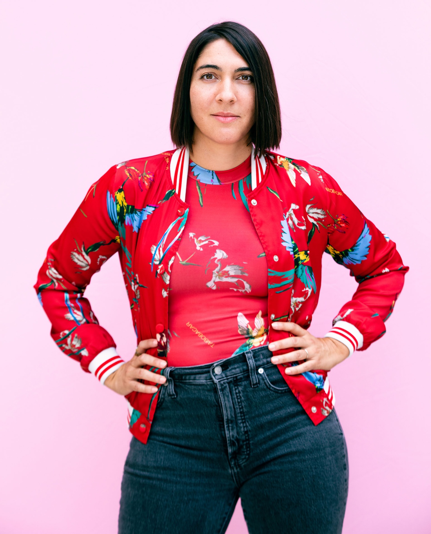 Image of Bridget Stokes with her hands on her hips, wearing a bright floral shirt with a pink background.