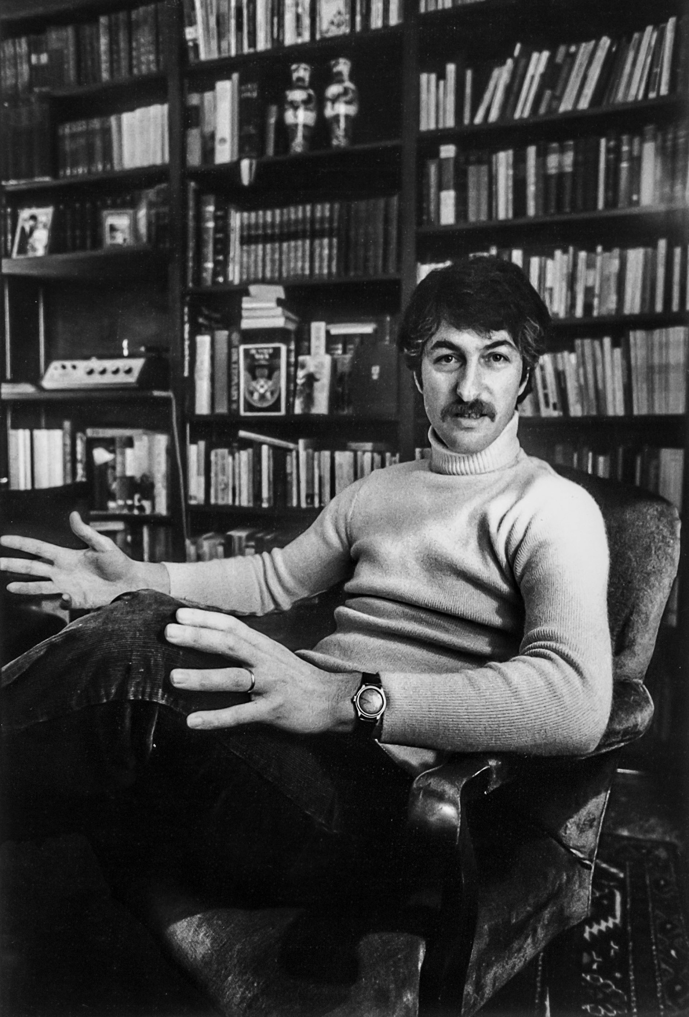 Black and white image of Arnold Weinstein sitting in a chair with books in the background in March 1974.