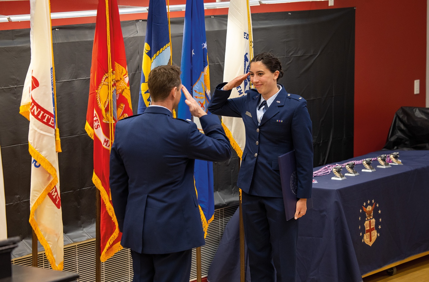 Image of Raquel Ruiter saluting an officer with flags in the background. 