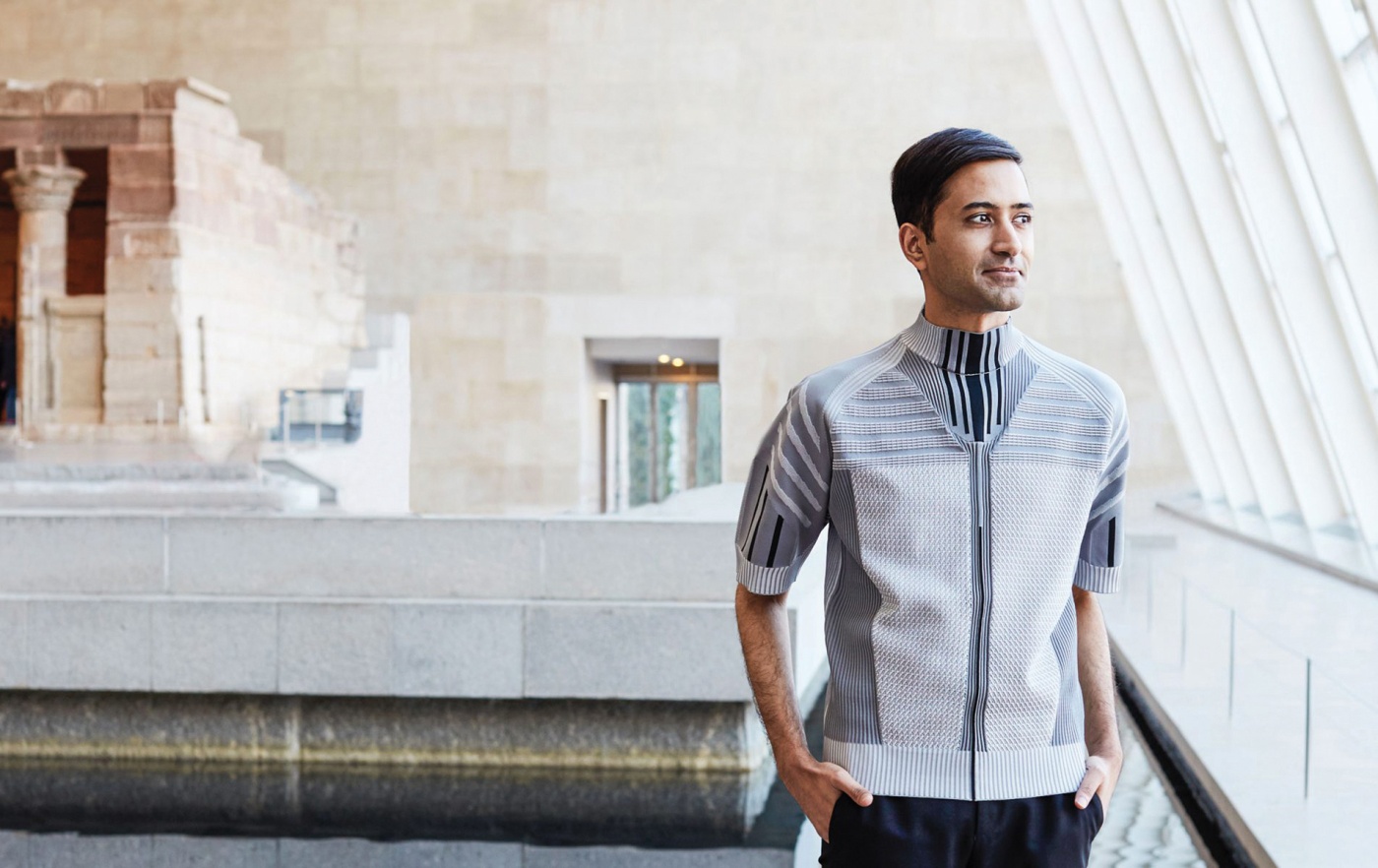 Image of Shanay Jhaveri standing in a gallery by a wall of windows looking out.