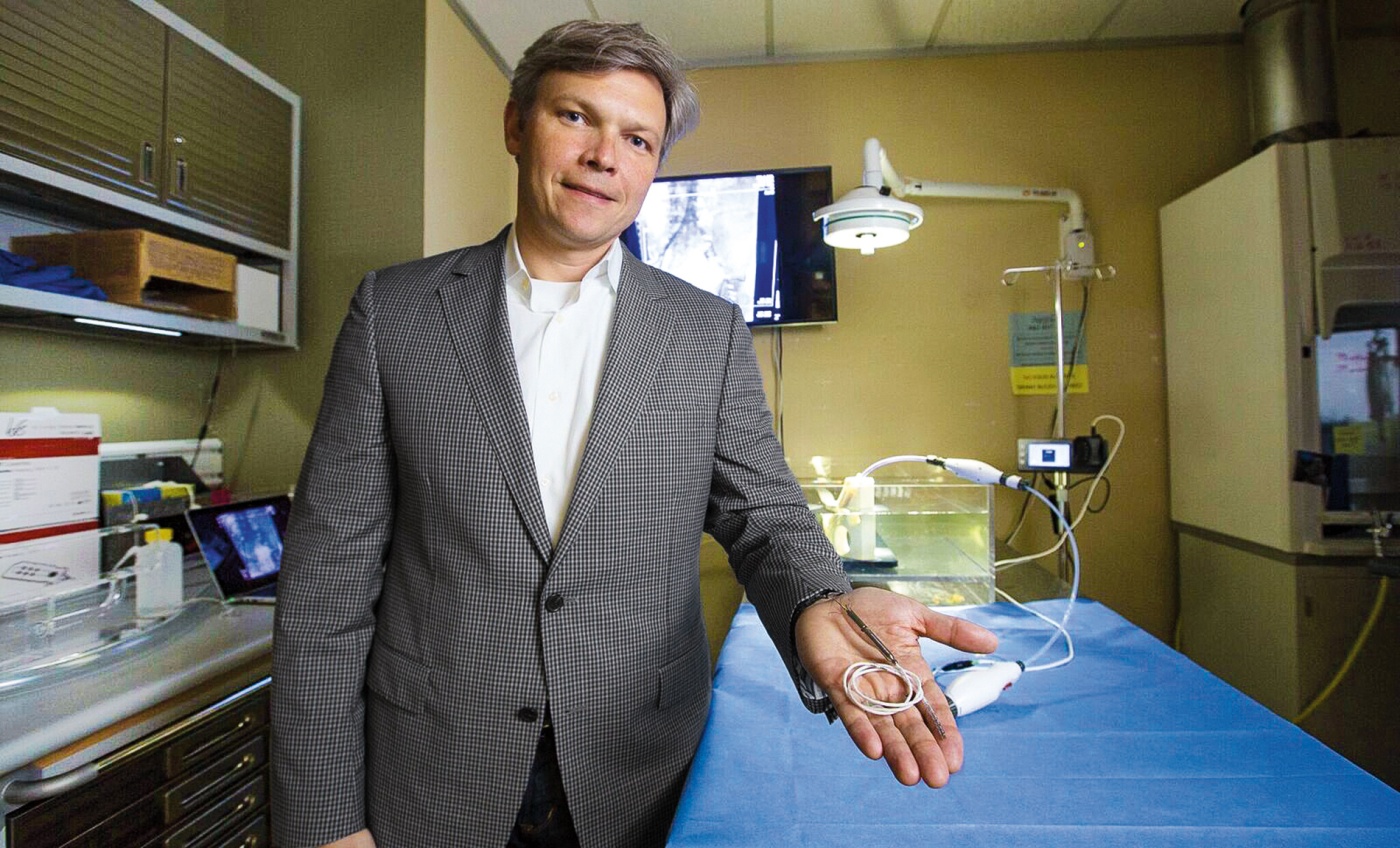 Image of Ben Herzog in a lab holding a heart pump in his outstretched hand.