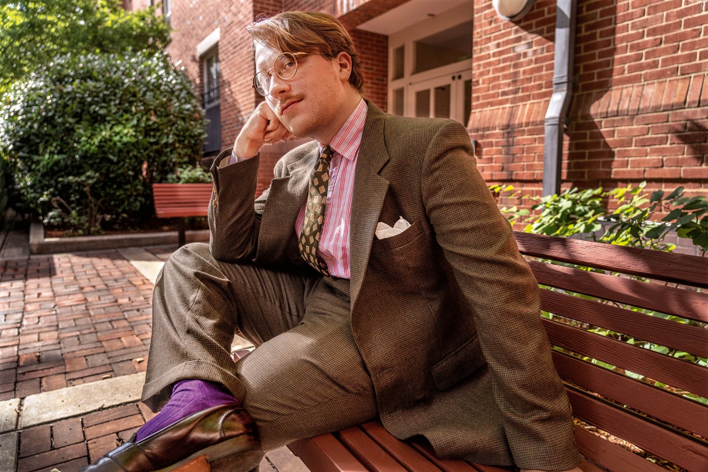 Image of Sean Toomey sitting on a bench on campus dressed in a vintage flannel suit.