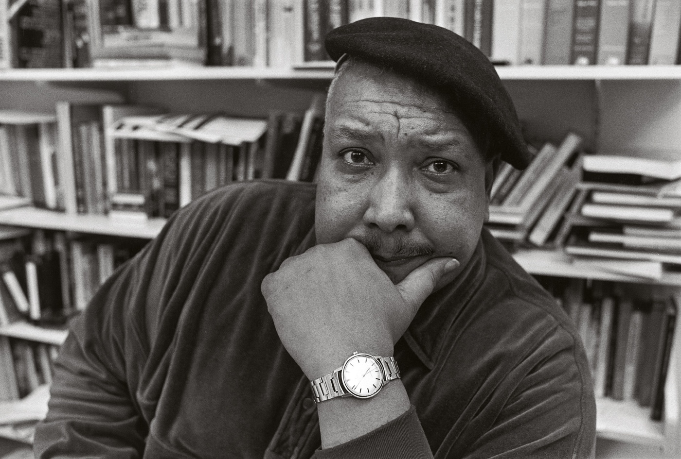 Archival image of Michael S. Harper with a beret on his head and books behind him.
