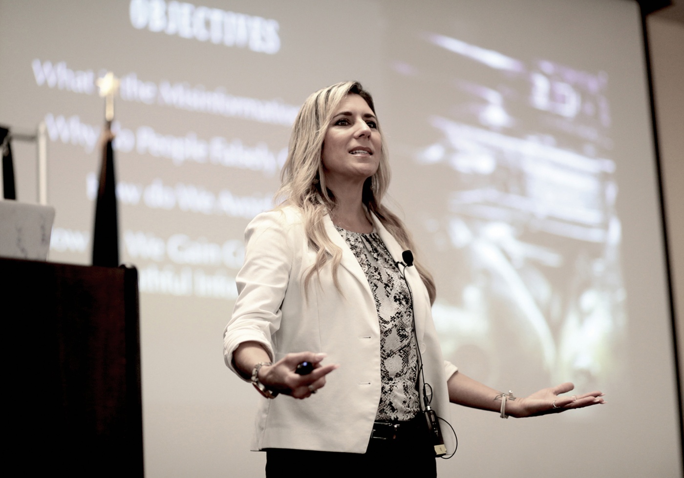 Imge of Lena Sisco speaking on stage with a screen behind her