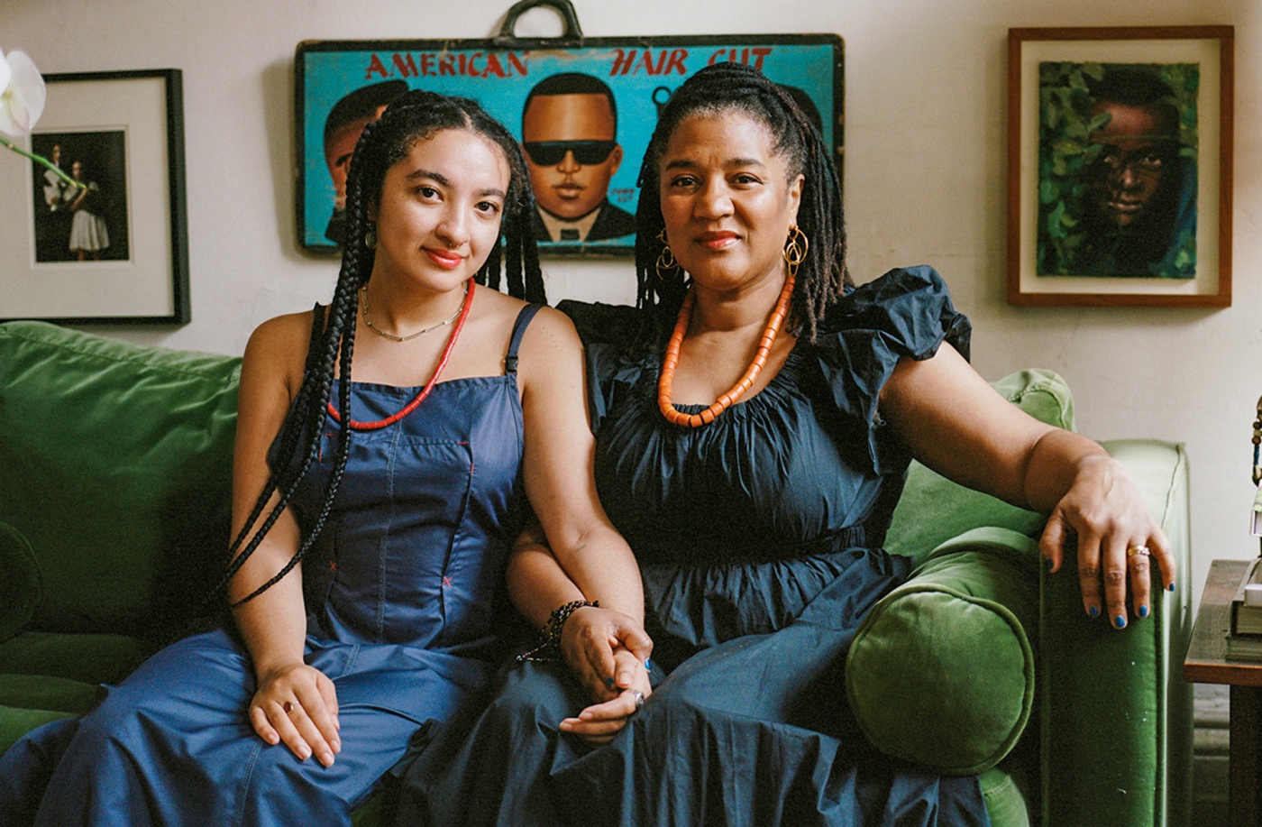 Image of Ruby Aiyo Gerber and her mother Lynn Nottage on a couch holding hands with paintings in the background.