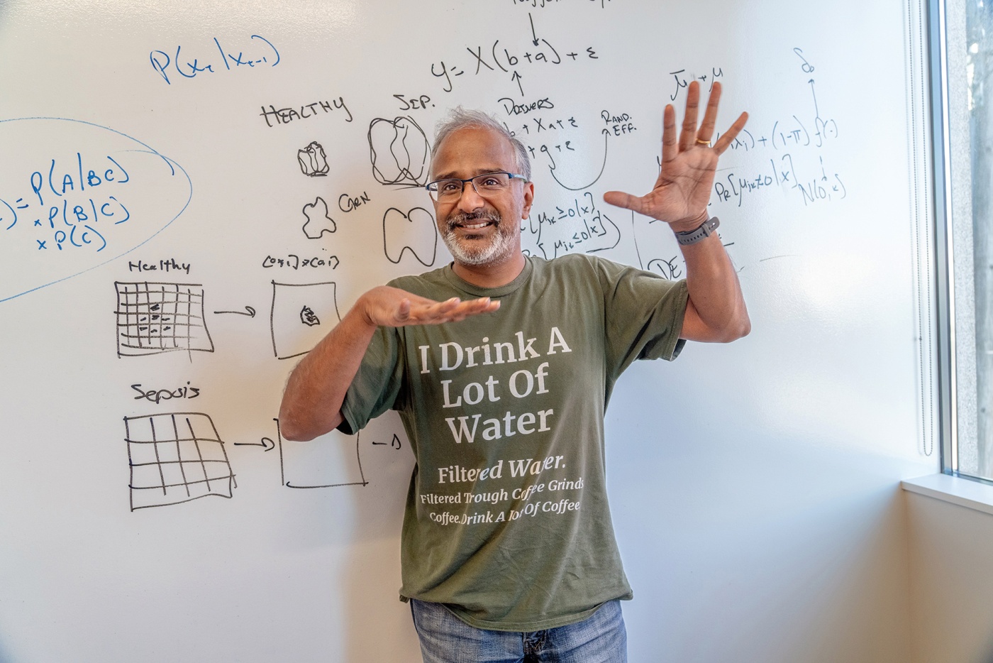 An image of Suresh Venkatasubramanian in front of a white board with hands wide