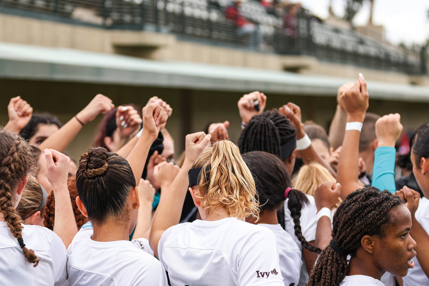 Image of women's soccer team holding their first high above in a team huddle.