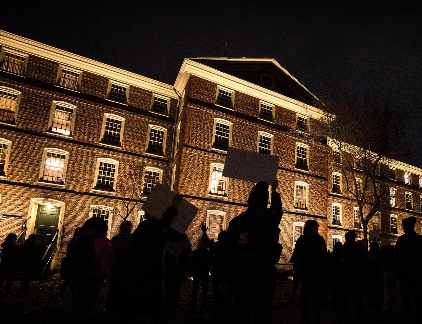 Image of students holding up signs and protesting at night in front of University Hall at Brown University