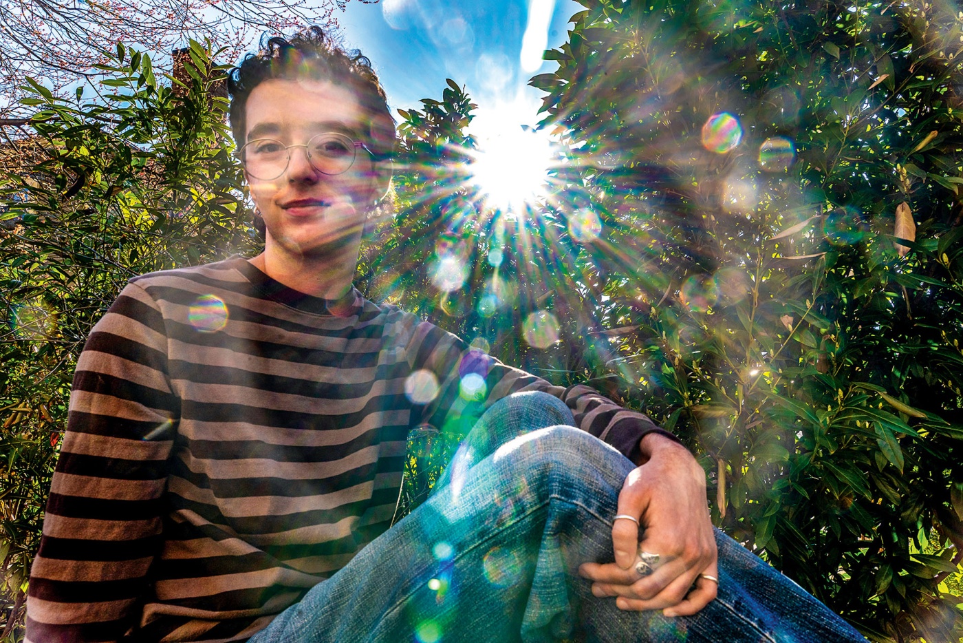 Image of Elliot Stravato sitting with his knee up and the sun shining through the trees