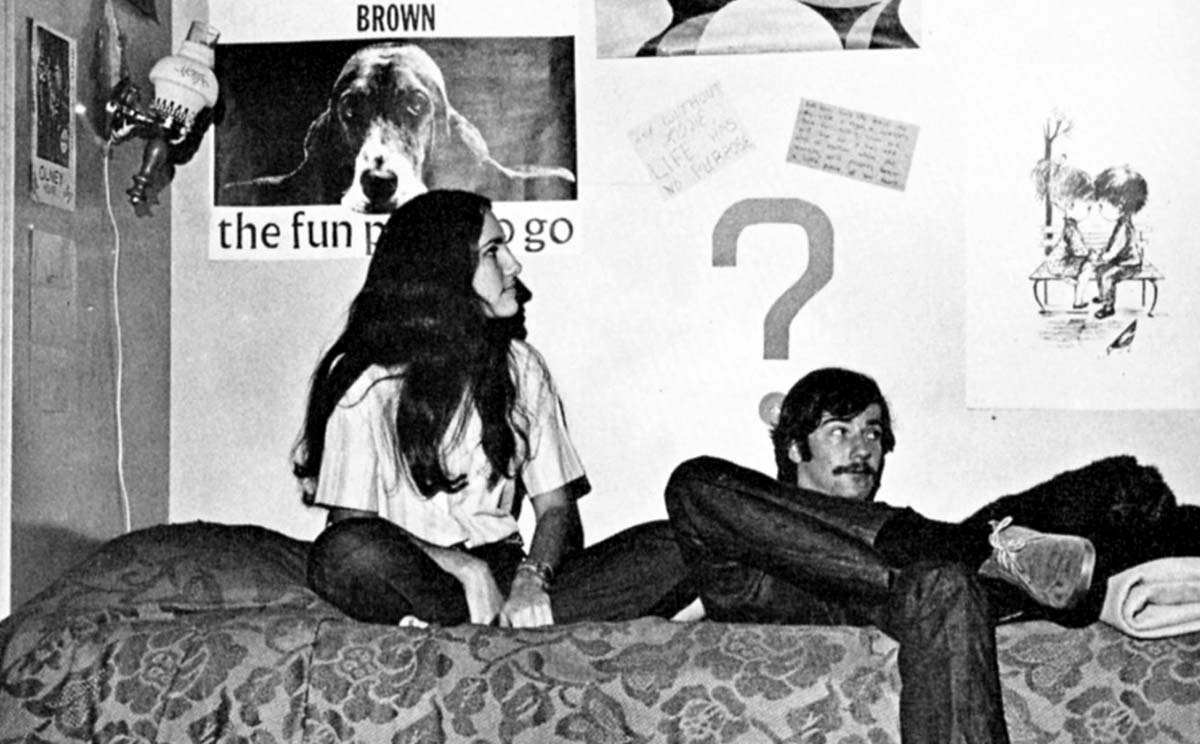 Archival image of two students sitting on a bed in a dorm room