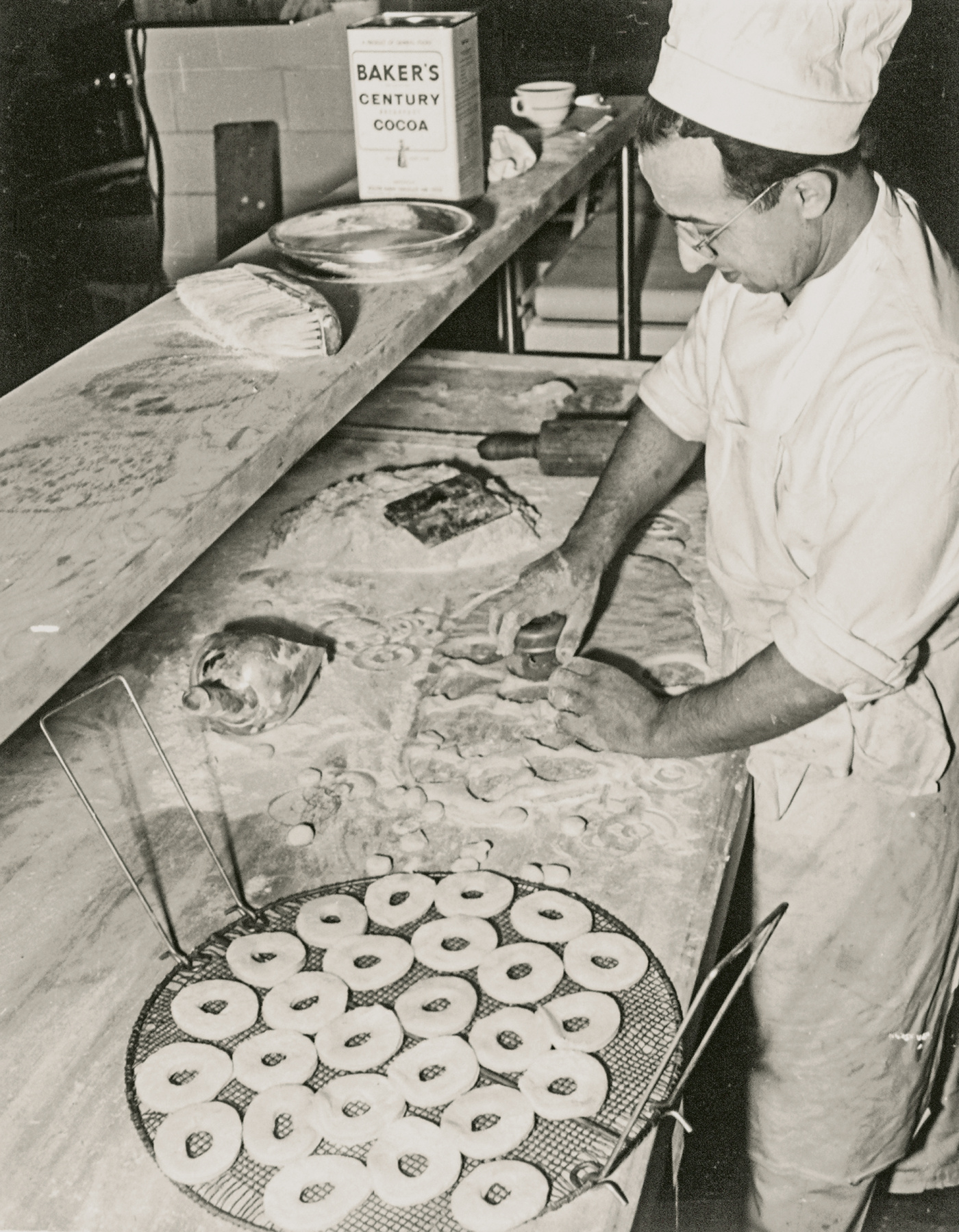 A baker cuts doughnuts in the 1950s