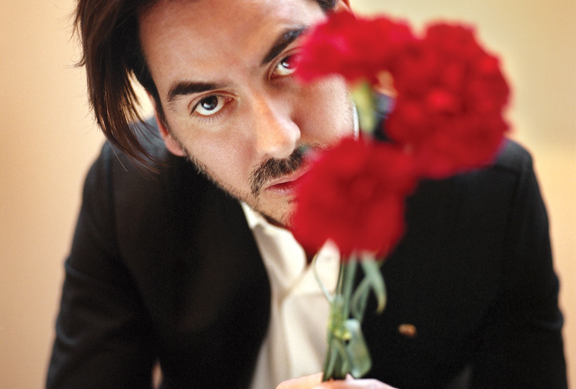 Image of Dhani Harrison ’01 in a black suit and white shirt, face partially obscured behind bright red flowers.