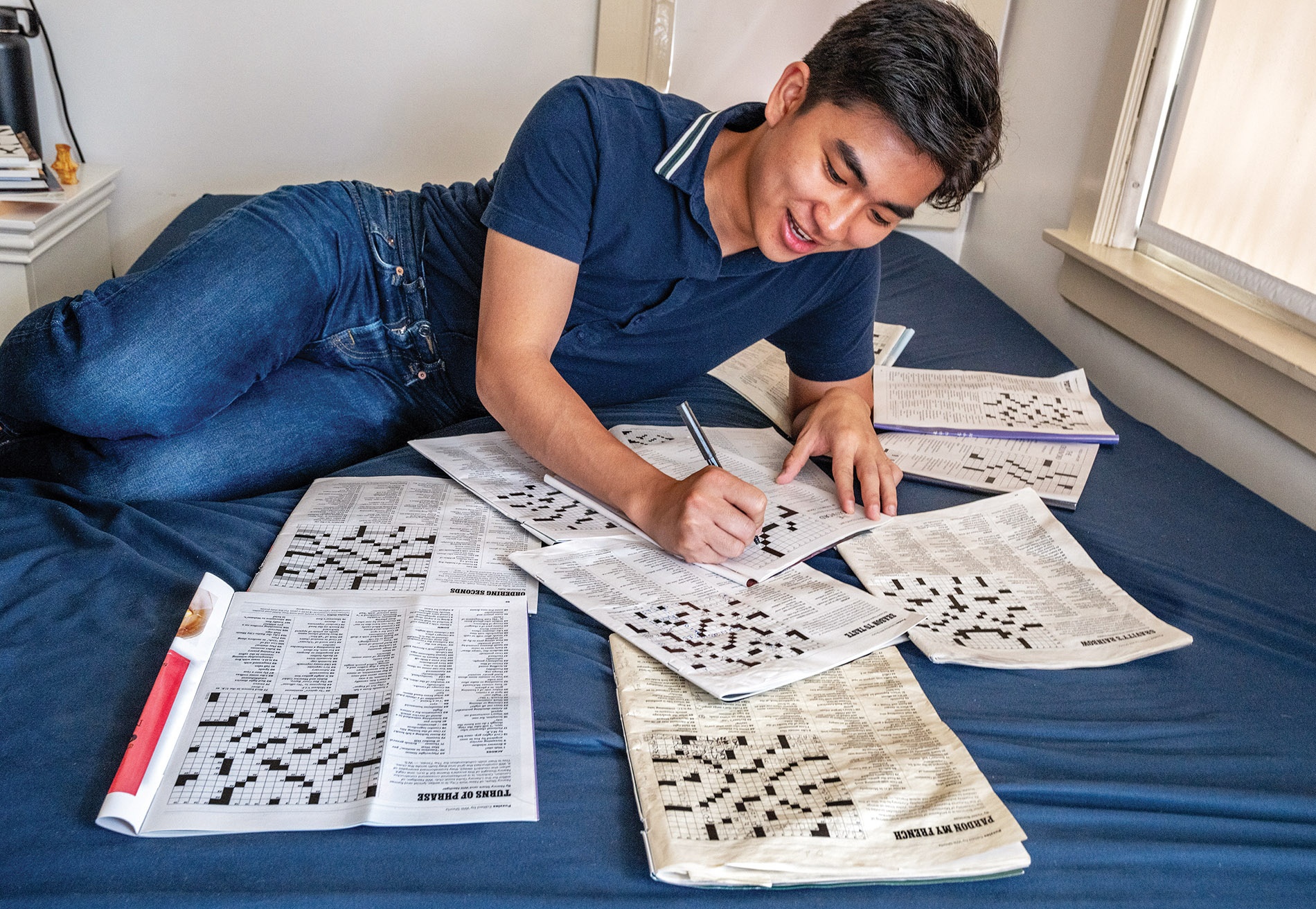 Image of Ethan Pan on his bed with crosswords surrounding him