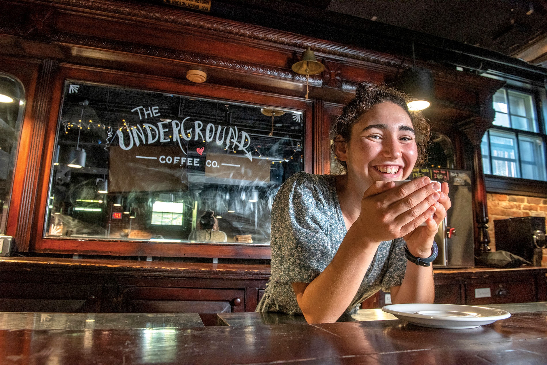 Image of Tevah Gevelber leaning on the bar with a cup of coffee in her hands