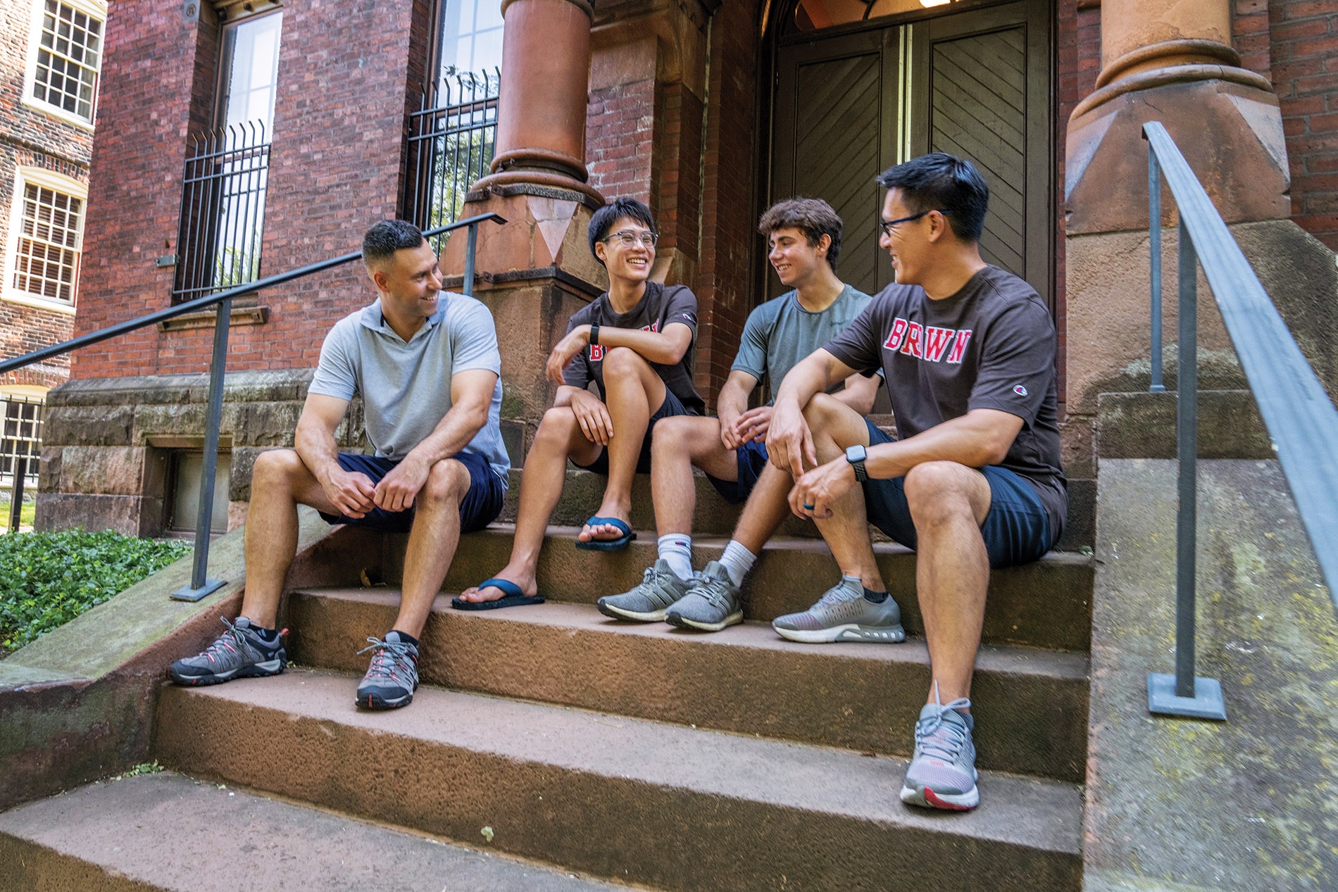 Image of two Brown alumni sitting on the steps on Brown campus with their two sons