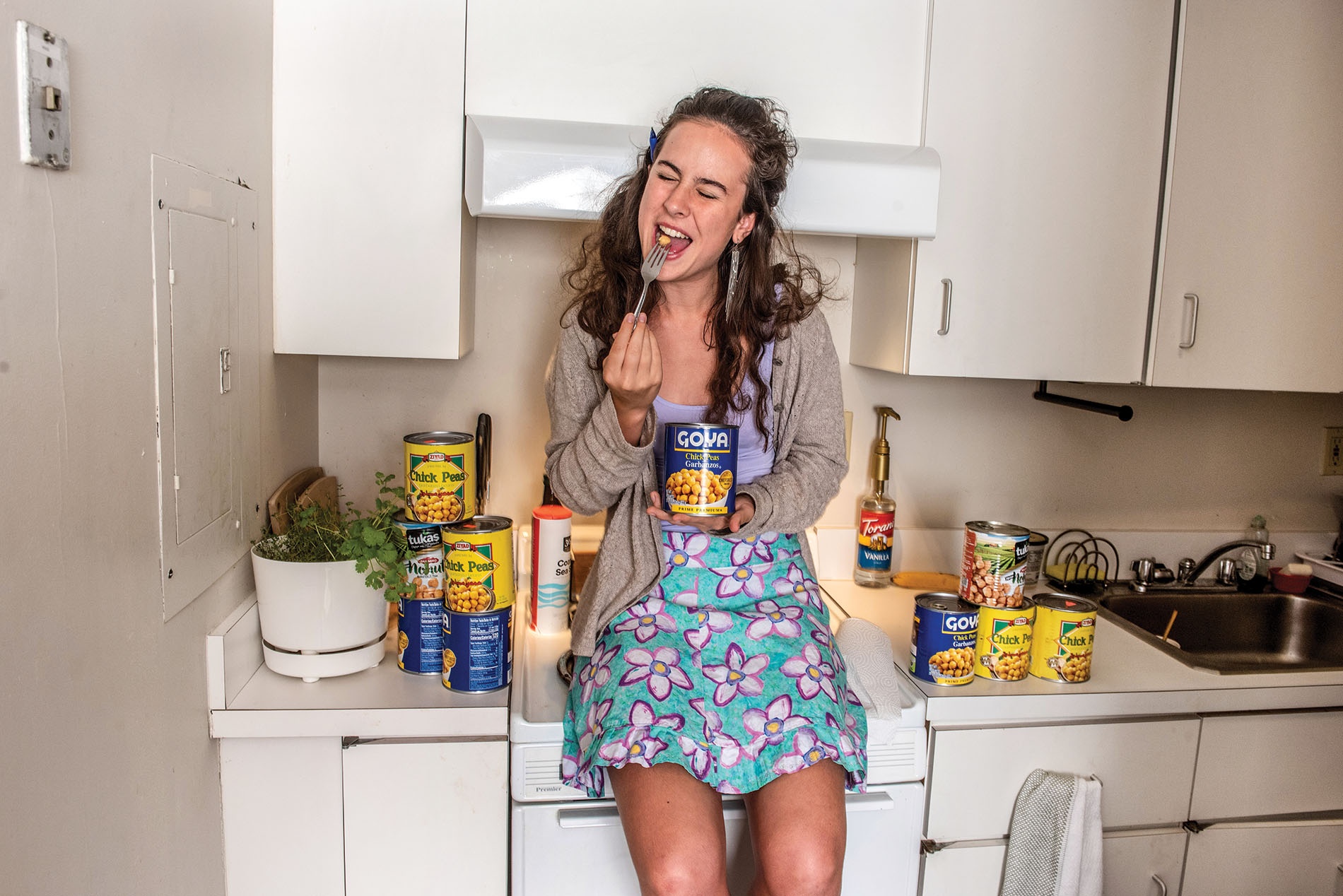 Image of Marielle Buxbaum sitting on the counter in her kitchen with cans of garbanzo beans.