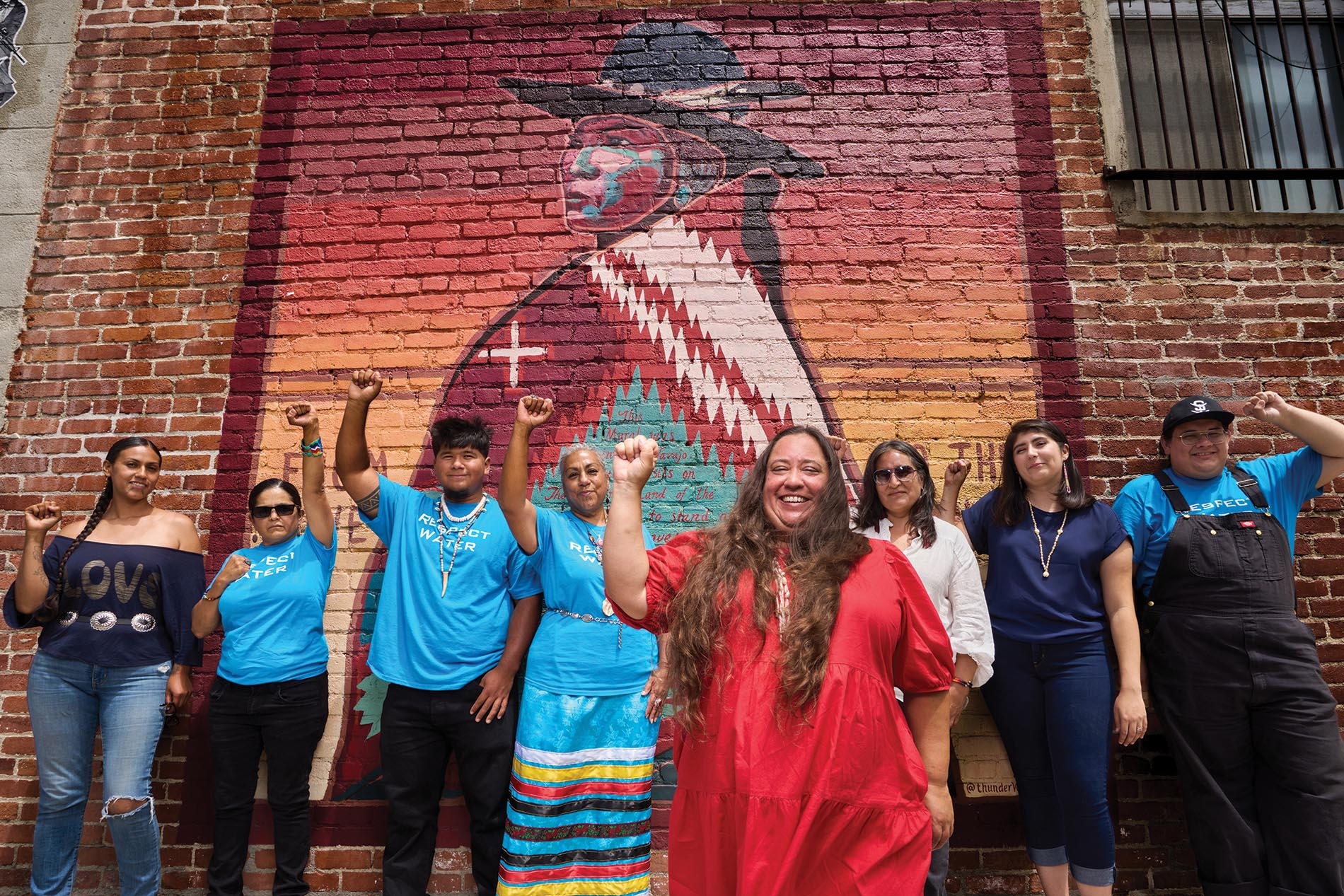 Image of Angela Mooney D'Arcy and staff holding their fists up in front of a mural on a brick wall.
