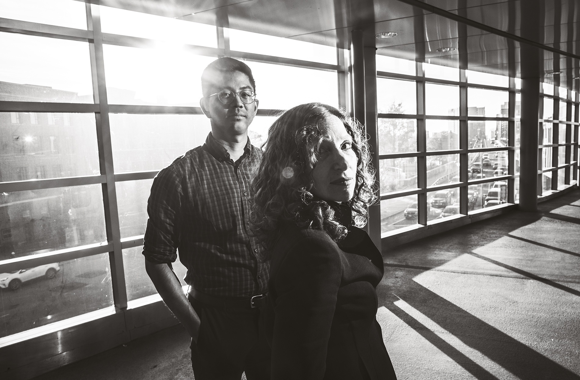 Image of Tony Thaweethai and Andrea Goldin Foulkes standing in front of a wall of windows looking at the camera.