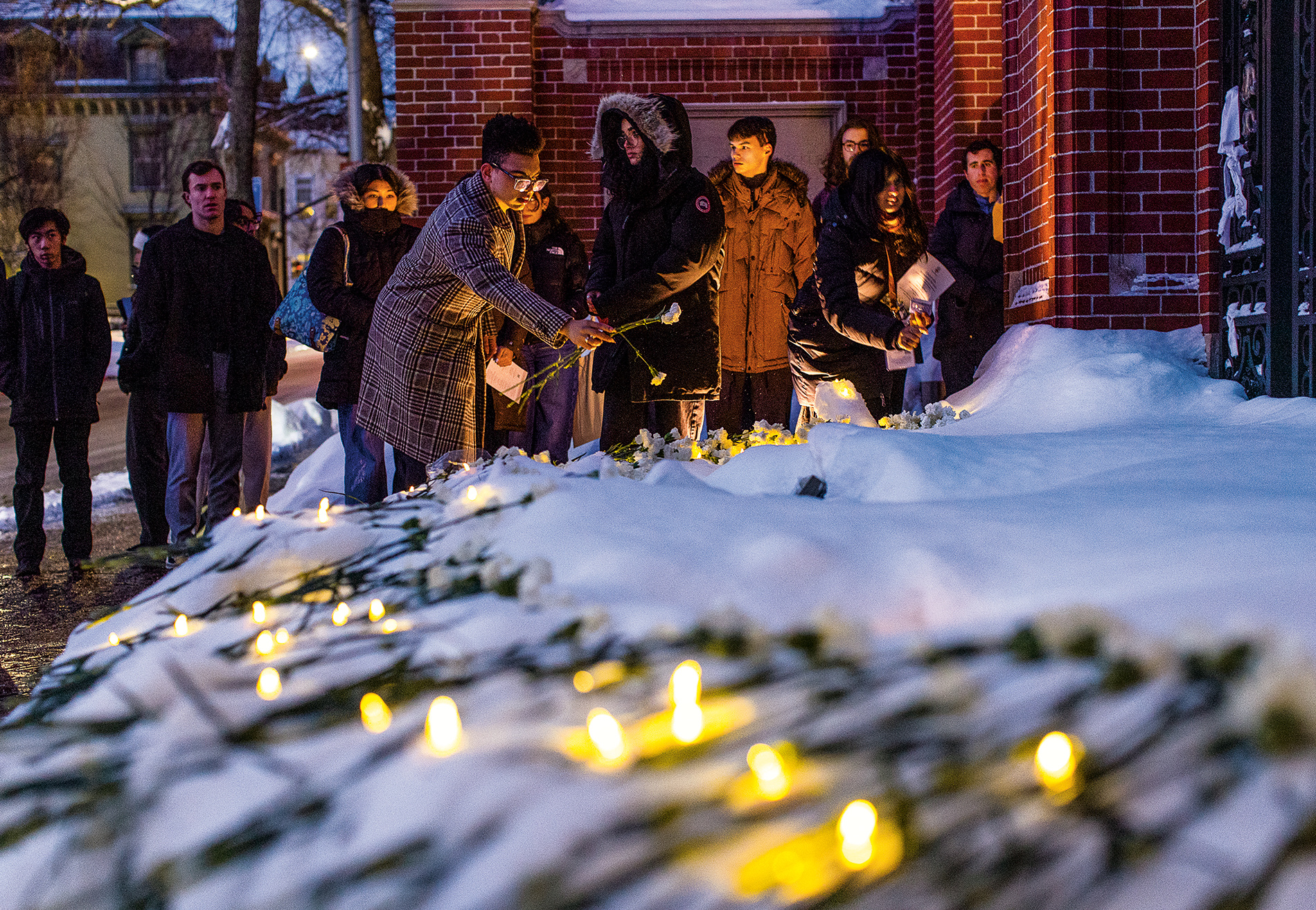 mourners leave flowers in the snow after a memorial service