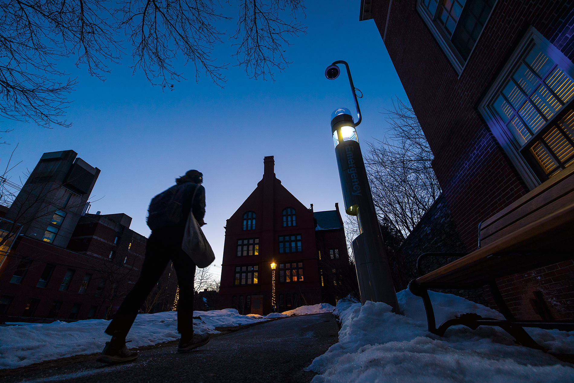 a student walks through campus lit by a security kiosk