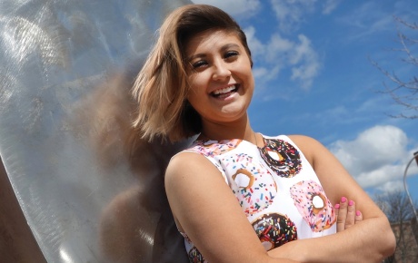 Photo of Rachael Cholak ’18 wearing a dress printed with donuts, in front of a large sculpture shaped like a donut.