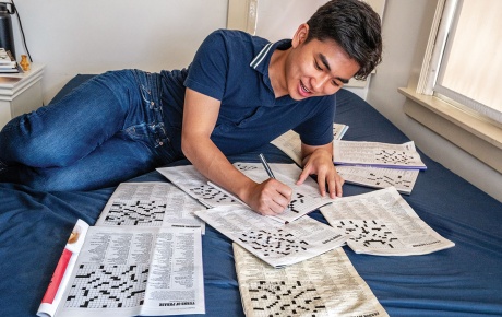 Image of Ethan Pan on his bed with crosswords surrounding him