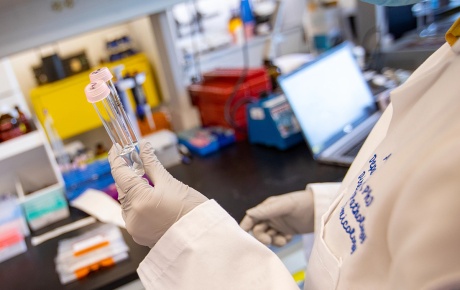 Image of a Brown researcher holding test tubes with a computer in the background.