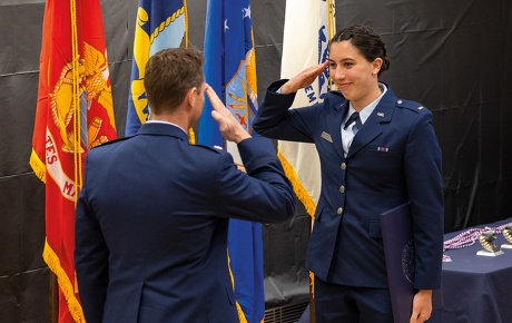 Image of Raquel Ruiter saluting an officer with flags in the background. 