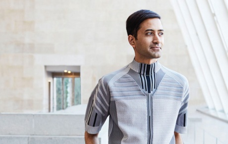 Image of Shanay Jhaveri standing in a gallery by a wall of windows looking out.