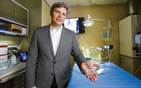 Image of Ben Herzog in a lab holding a heart pump in his outstretched hand.