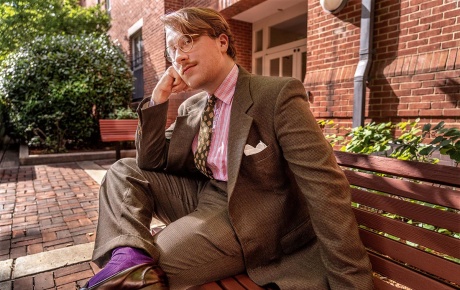 Image of Sean Toomey sitting on a bench on campus dressed in a vintage flannel suit.