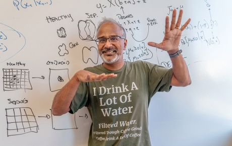 An image of Suresh Venkatasubramanian in front of a white board with hands wide