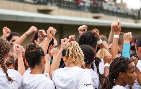 Image of women's soccer team holding their first high above in a team huddle.