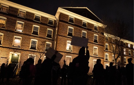 Image of students holding up signs and protesting at night in front of University Hall at Brown University